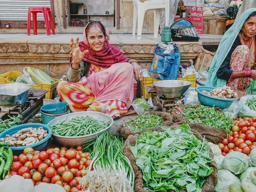 A woman at her vegetable stall, hand raised