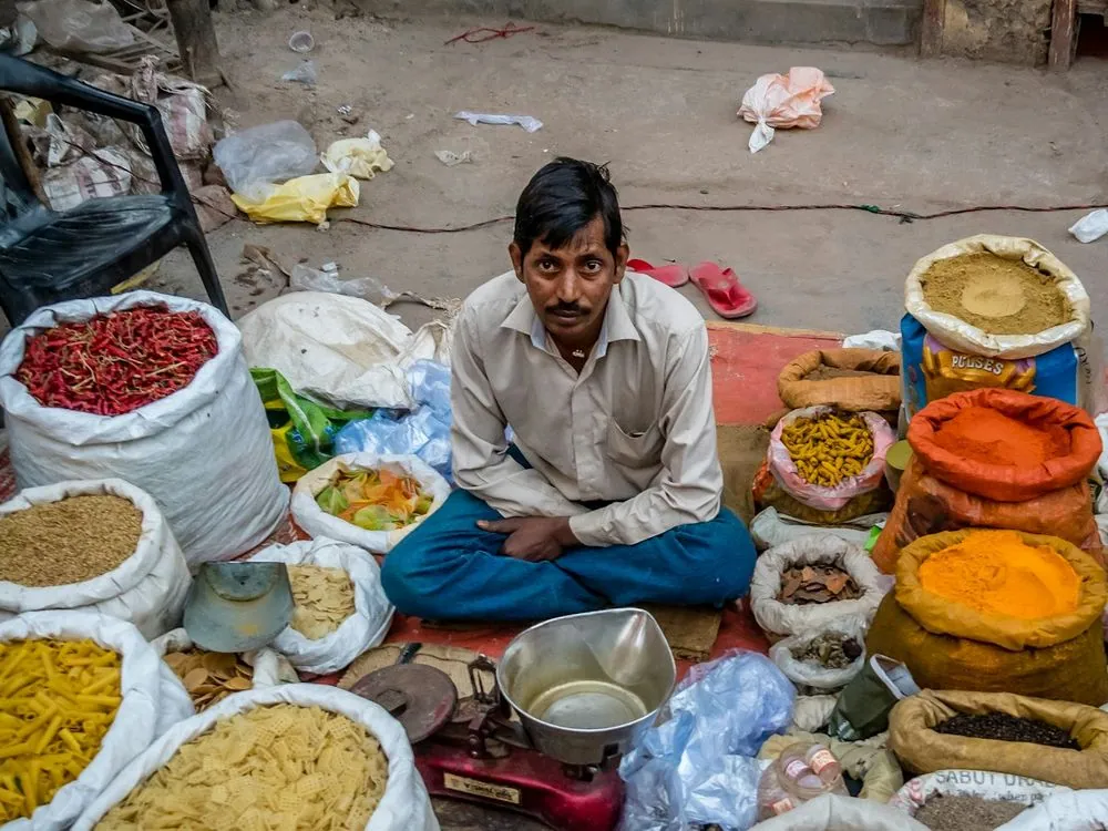 A trader seated among open sacks of spices and pulses