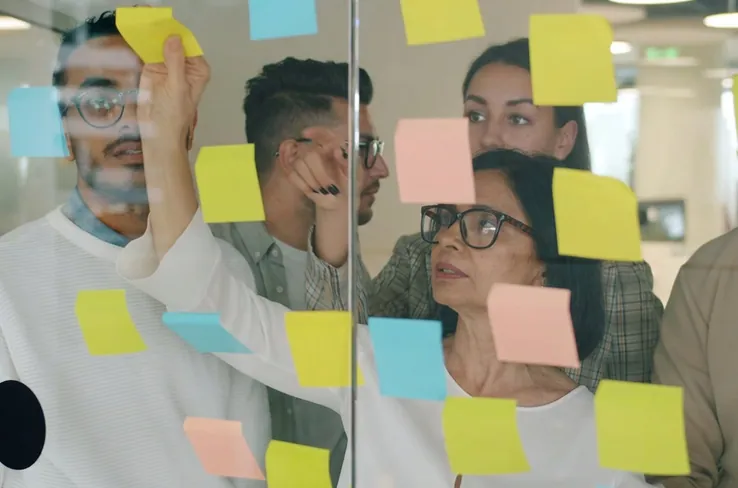 People adding sticky notes to a glass wall