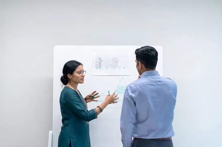 A woman presenting at a whiteboard to a colleague
