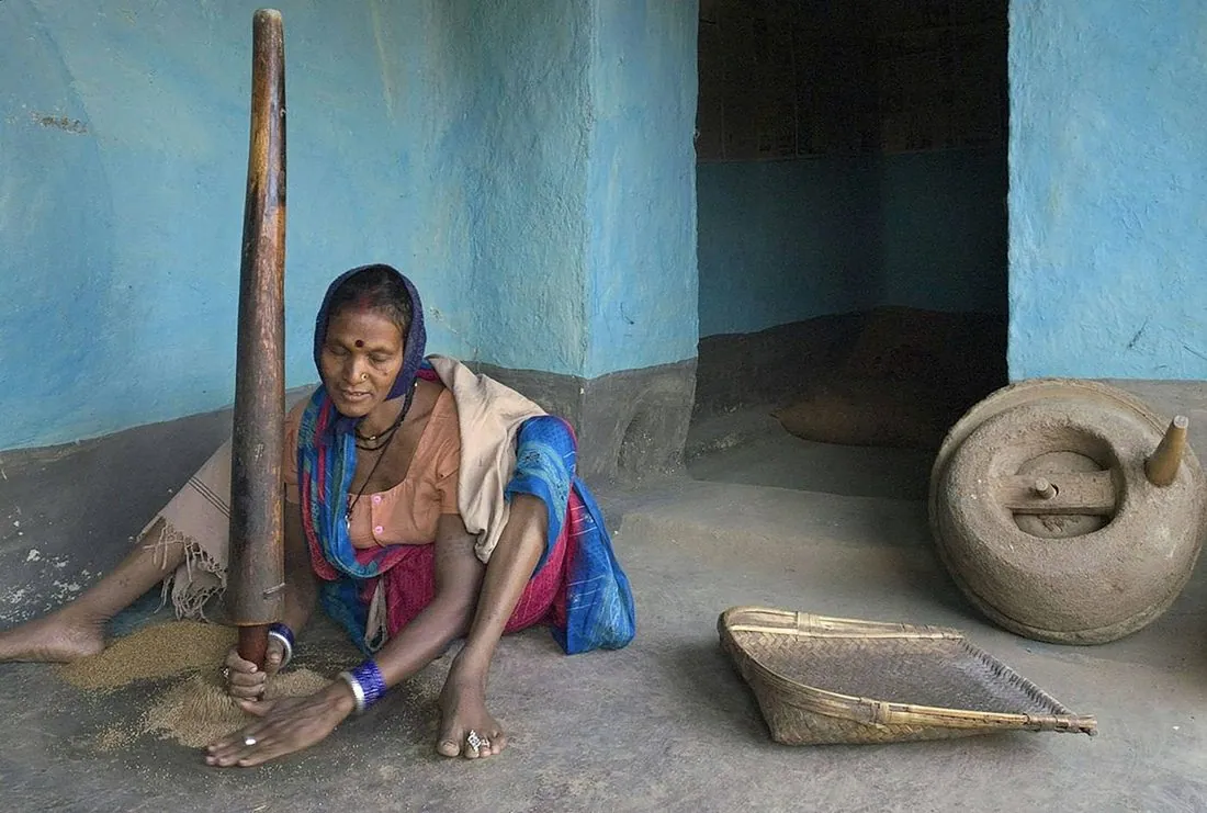 A woman grinding grain outside her home