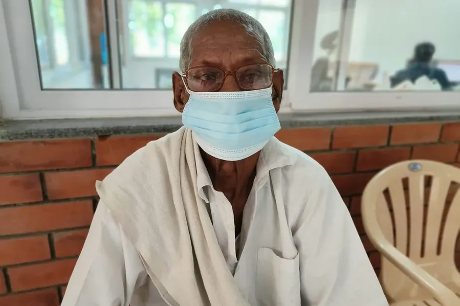 An older man seated indoors wearing a mask