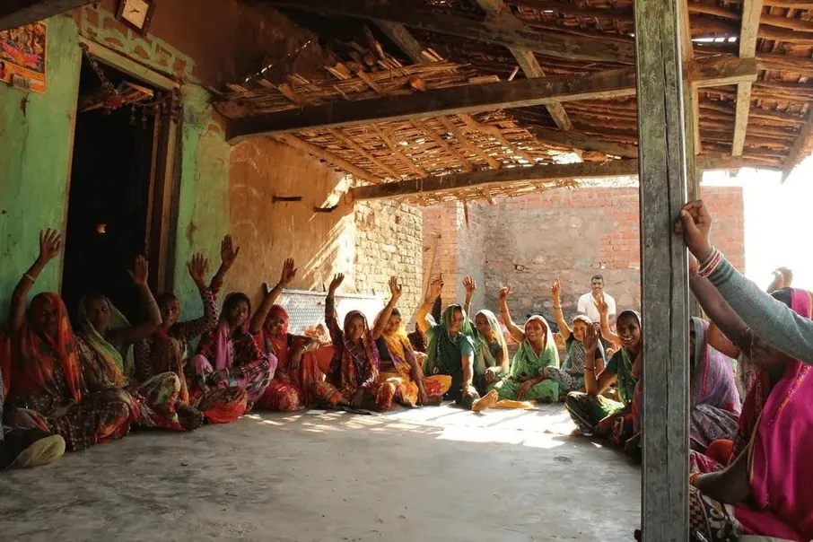 Women seated on the floor of a hall, hands raised