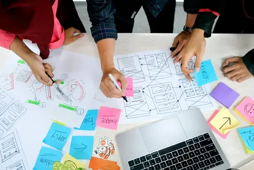 Hands sketching screen layouts among sticky notes