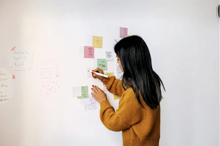 A woman writing on a wall of sticky notes