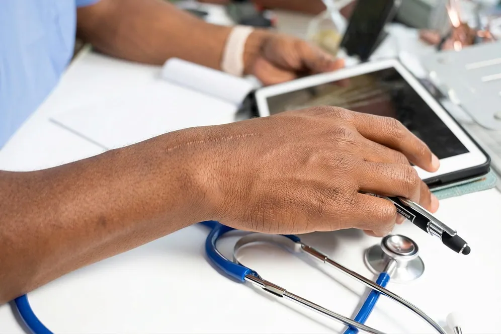 A health worker writing on a clipboard beside a tablet
